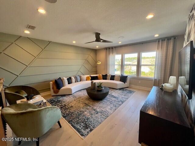 living room with ceiling fan, a textured ceiling, and light hardwood / wood-style floors