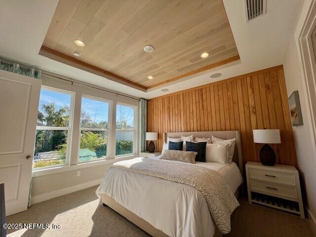 carpeted bedroom with wooden walls, a raised ceiling, and wooden ceiling