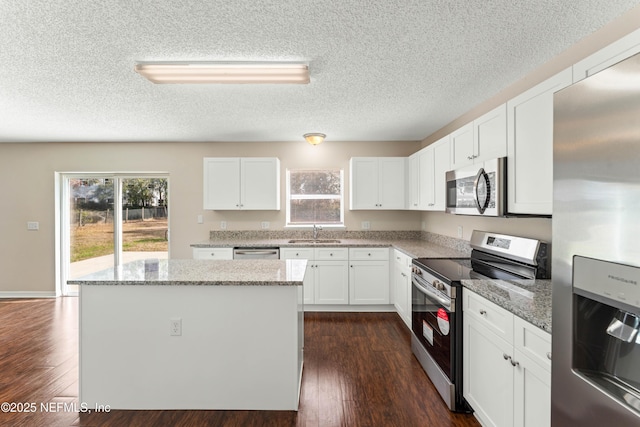 kitchen featuring appliances with stainless steel finishes, sink, white cabinets, a center island, and light stone counters