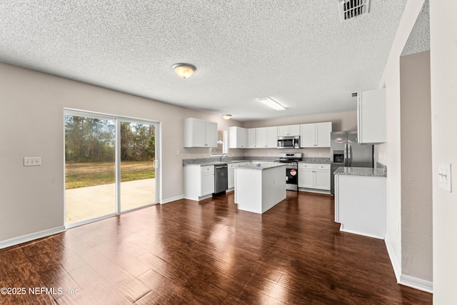 kitchen with appliances with stainless steel finishes, light stone counters, white cabinets, a kitchen island, and dark hardwood / wood-style flooring