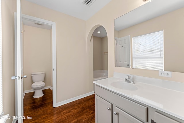 bathroom with hardwood / wood-style flooring, a tub to relax in, toilet, and vanity