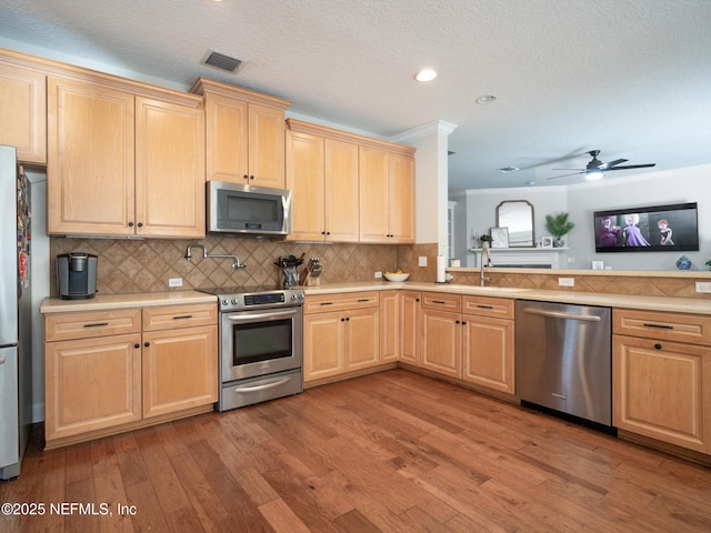 kitchen with stainless steel appliances, light brown cabinetry, hardwood / wood-style floors, and decorative backsplash