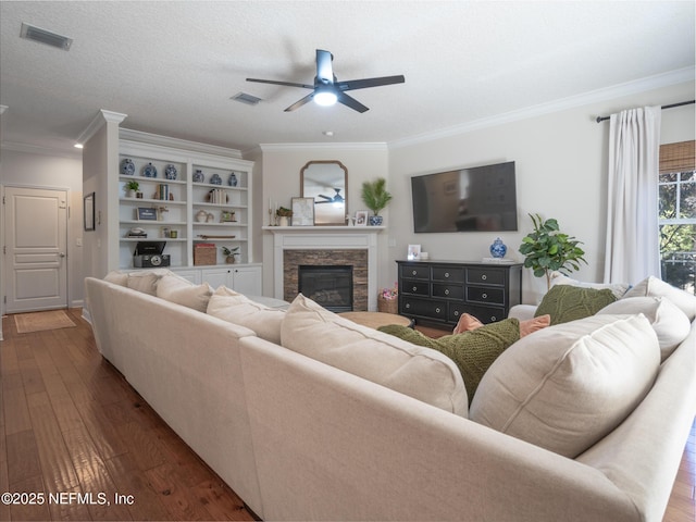 living room featuring dark wood-type flooring, a stone fireplace, a textured ceiling, ornamental molding, and ceiling fan