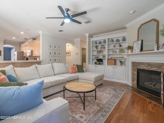 living room featuring ceiling fan, a fireplace, ornamental molding, a textured ceiling, and dark hardwood / wood-style flooring