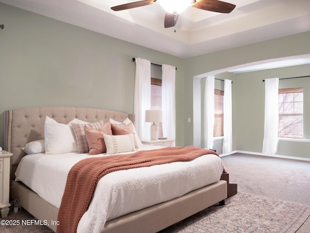 carpeted bedroom featuring ceiling fan and a raised ceiling