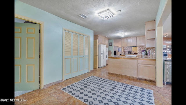 kitchen featuring sink, white refrigerator with ice dispenser, a textured ceiling, and light brown cabinets