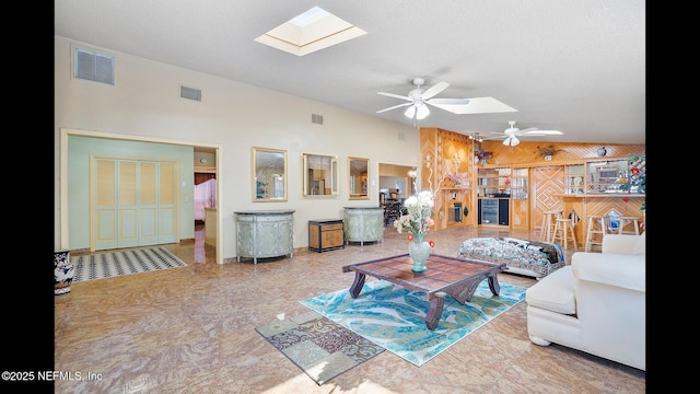 living room featuring ceiling fan, a textured ceiling, and vaulted ceiling with skylight