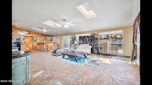 living room featuring ceiling fan, vaulted ceiling with skylight, and a textured ceiling