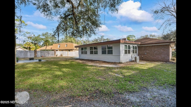 rear view of house with central AC unit and a lawn