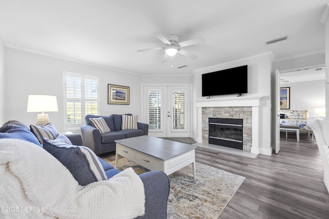 living room with a stone fireplace, hardwood / wood-style flooring, ornamental molding, ceiling fan, and french doors