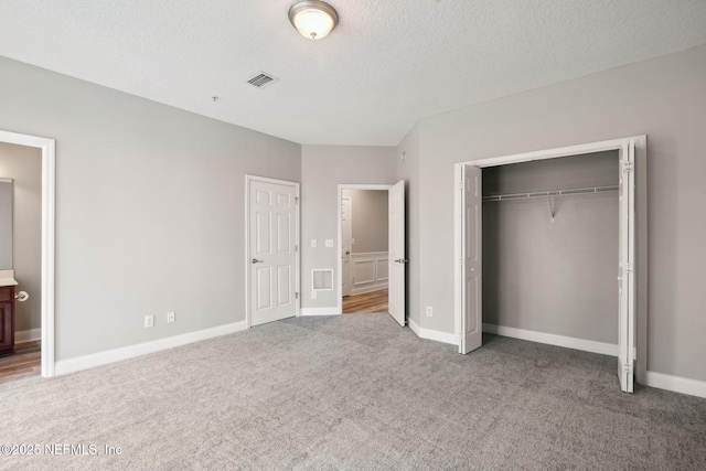 unfurnished bedroom featuring ensuite bathroom, carpet flooring, a closet, and a textured ceiling