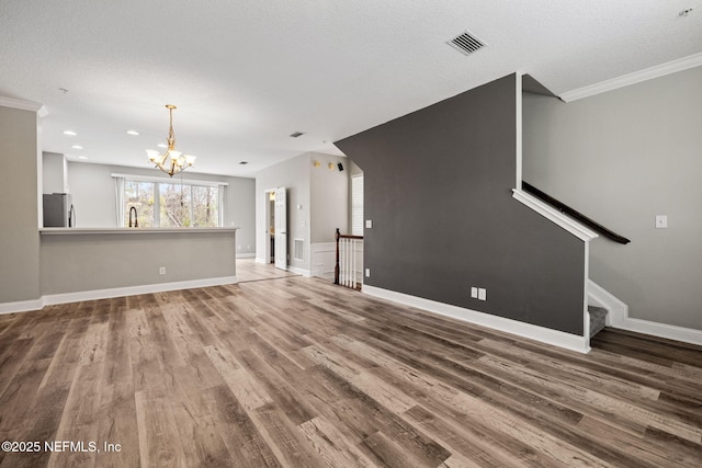 unfurnished living room featuring sink, an inviting chandelier, crown molding, wood-type flooring, and a textured ceiling