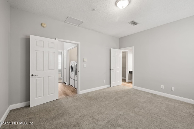 unfurnished bedroom featuring washing machine and dryer, light carpet, and a textured ceiling