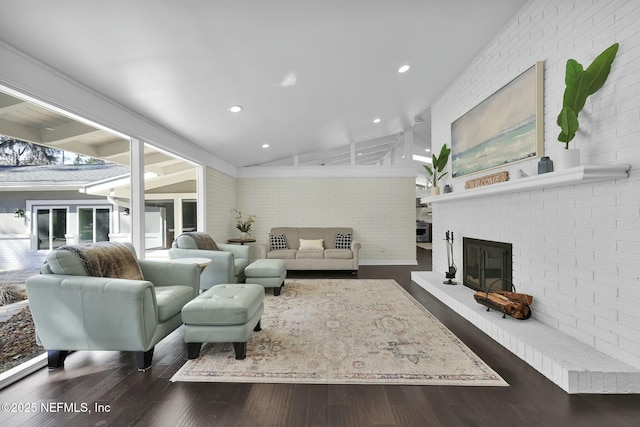 living room featuring lofted ceiling, brick wall, a fireplace, and dark hardwood / wood-style flooring