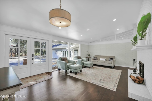 living room with lofted ceiling, a fireplace, brick wall, dark hardwood / wood-style flooring, and french doors