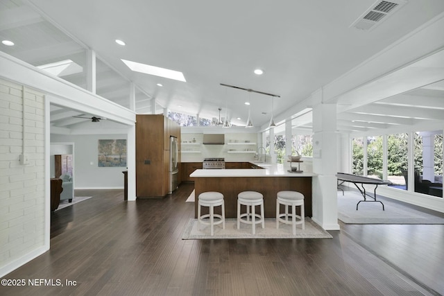 kitchen featuring lofted ceiling with skylight, decorative light fixtures, dark hardwood / wood-style flooring, stainless steel appliances, and wall chimney range hood