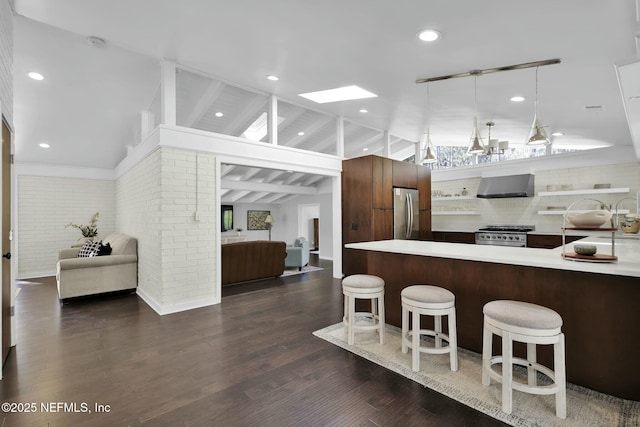 kitchen featuring stainless steel appliances, lofted ceiling with skylight, hanging light fixtures, brick wall, and wall chimney range hood