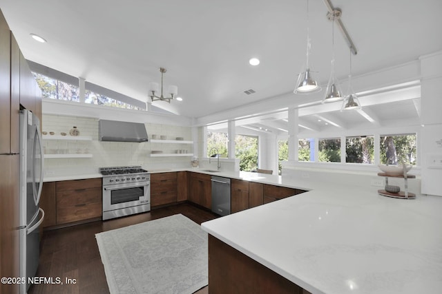 kitchen with lofted ceiling, wall chimney range hood, appliances with stainless steel finishes, plenty of natural light, and decorative light fixtures