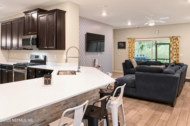 kitchen with a breakfast bar area, dark brown cabinets, light wood-type flooring, kitchen peninsula, and stainless steel appliances