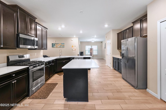 kitchen with sink, appliances with stainless steel finishes, dark brown cabinets, a kitchen island, and a kitchen bar