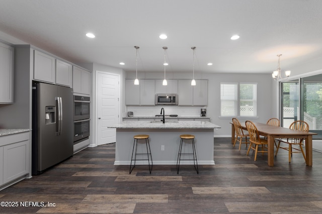 kitchen with pendant lighting, appliances with stainless steel finishes, light stone countertops, and an island with sink