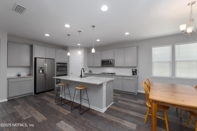 kitchen with a kitchen island with sink, decorative light fixtures, stainless steel appliances, and gray cabinetry