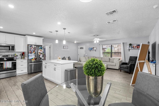 kitchen with hanging light fixtures, appliances with stainless steel finishes, a kitchen island, decorative backsplash, and white cabinets