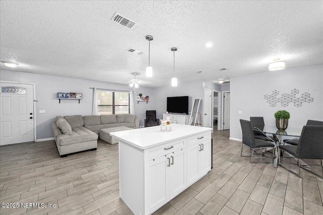 kitchen with white cabinetry, a center island, a textured ceiling, and decorative light fixtures