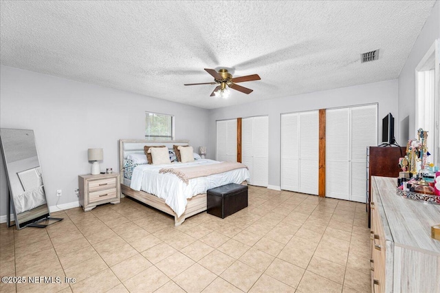 tiled bedroom with ceiling fan, a textured ceiling, and two closets