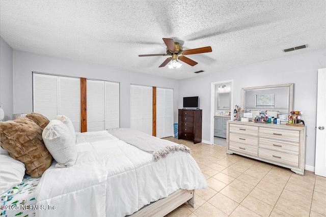 bedroom with ensuite bathroom, light tile patterned floors, ceiling fan, multiple closets, and a textured ceiling