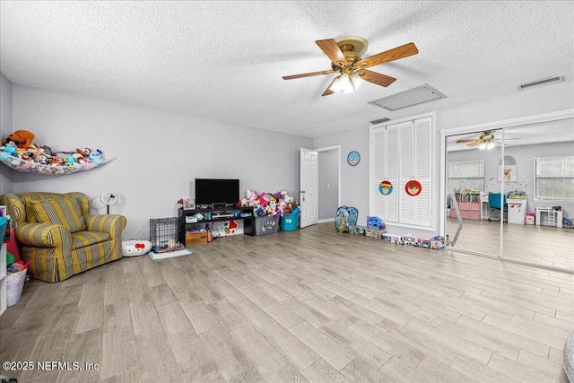 recreation room with a textured ceiling, ceiling fan, and light wood-type flooring