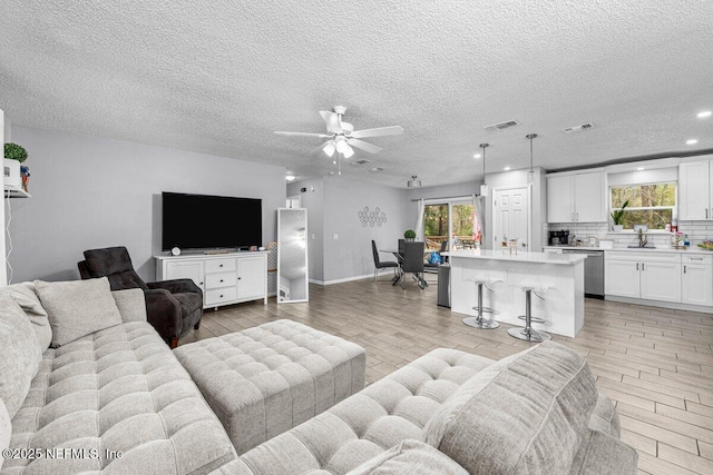 living room with ceiling fan, sink, light hardwood / wood-style floors, and a textured ceiling