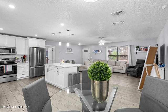 kitchen with white cabinetry, hanging light fixtures, appliances with stainless steel finishes, a kitchen island, and backsplash