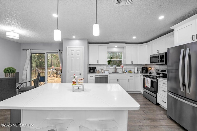 kitchen featuring a kitchen island, appliances with stainless steel finishes, decorative light fixtures, white cabinetry, and sink