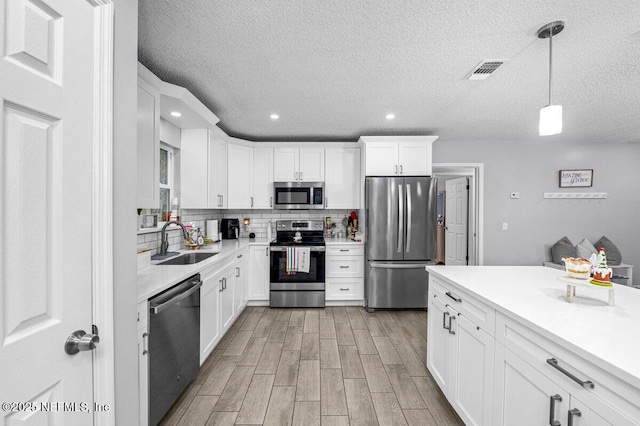 kitchen with appliances with stainless steel finishes, white cabinetry, sink, hanging light fixtures, and light hardwood / wood-style flooring