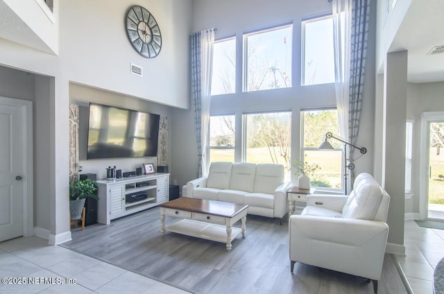 living area featuring baseboards, a high ceiling, visible vents, and light wood-style floors