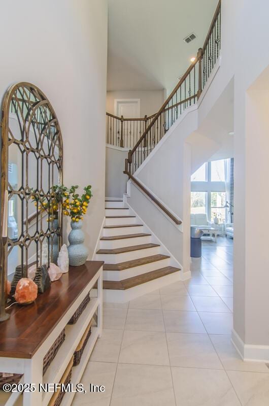 entryway featuring light tile patterned floors, baseboards, visible vents, a towering ceiling, and stairs