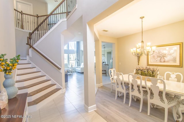 dining room with visible vents, a towering ceiling, an inviting chandelier, baseboards, and stairs