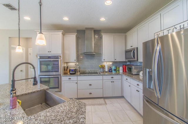 kitchen featuring light stone counters, decorative light fixtures, appliances with stainless steel finishes, white cabinets, and wall chimney range hood