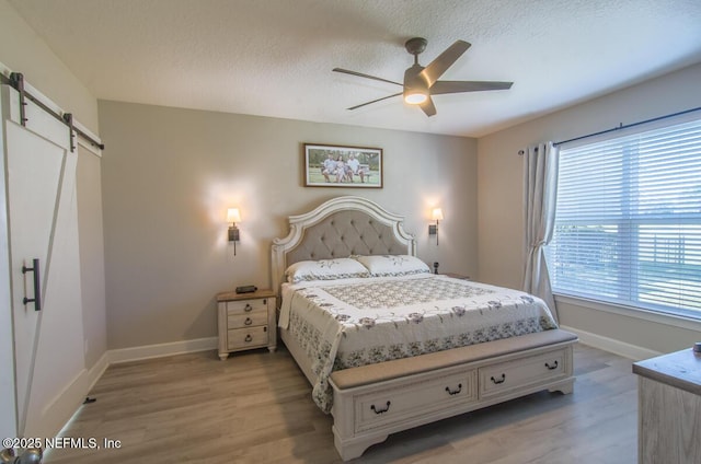 bedroom with light wood finished floors, a barn door, and baseboards