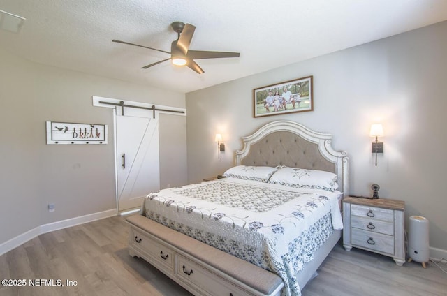 bedroom with a closet, a barn door, ceiling fan, light wood-type flooring, and baseboards