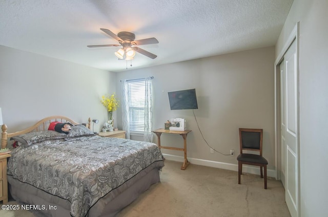 bedroom featuring ceiling fan, a textured ceiling, light colored carpet, baseboards, and a closet