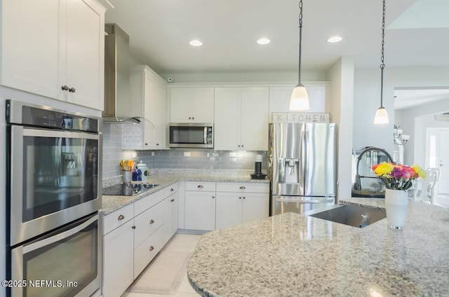 kitchen with white cabinets, stainless steel appliances, backsplash, wall chimney range hood, and hanging light fixtures
