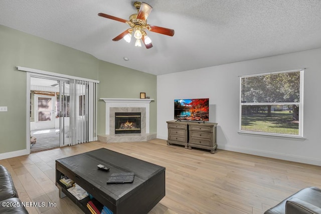 living room with vaulted ceiling, a fireplace, ceiling fan, a textured ceiling, and light hardwood / wood-style flooring