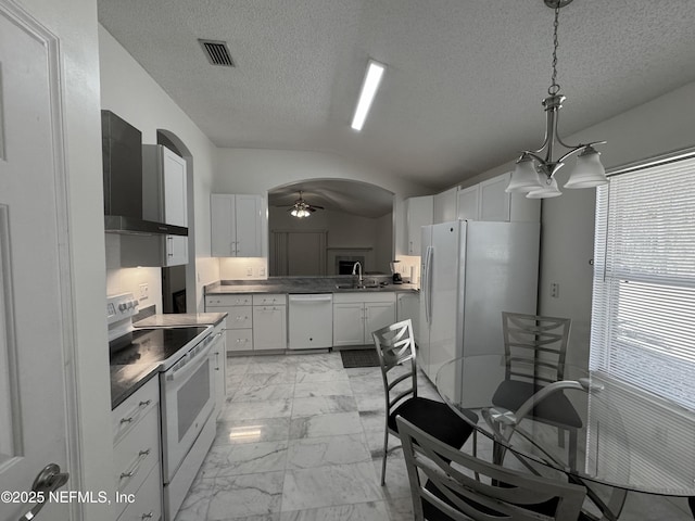 kitchen featuring sink, white cabinets, hanging light fixtures, wall chimney range hood, and white appliances