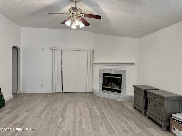 unfurnished living room featuring a textured ceiling, a premium fireplace, ceiling fan, and light wood-type flooring