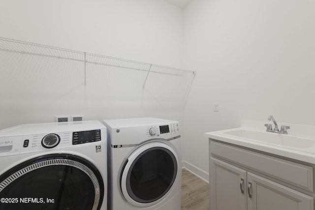 laundry room featuring cabinets, washing machine and dryer, sink, and light hardwood / wood-style flooring