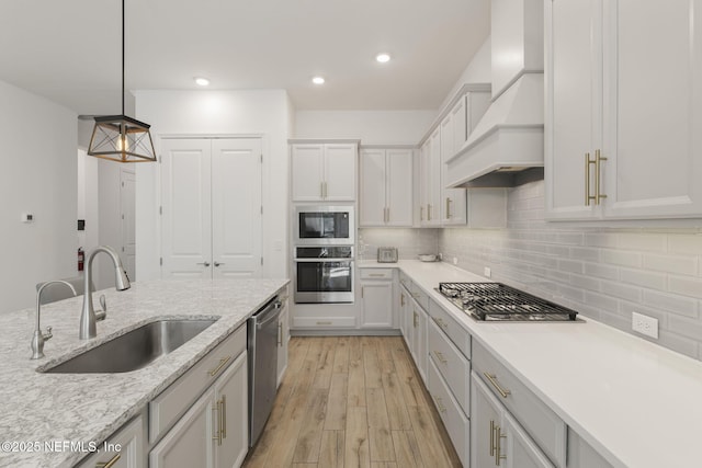 kitchen featuring sink, light stone counters, decorative light fixtures, custom range hood, and stainless steel appliances