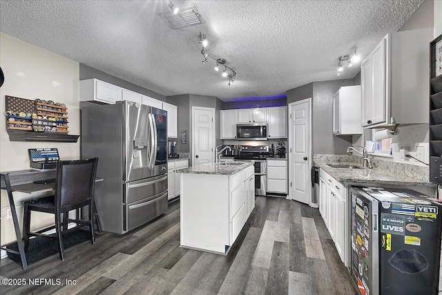 kitchen with white cabinetry, sink, stainless steel appliances, and an island with sink