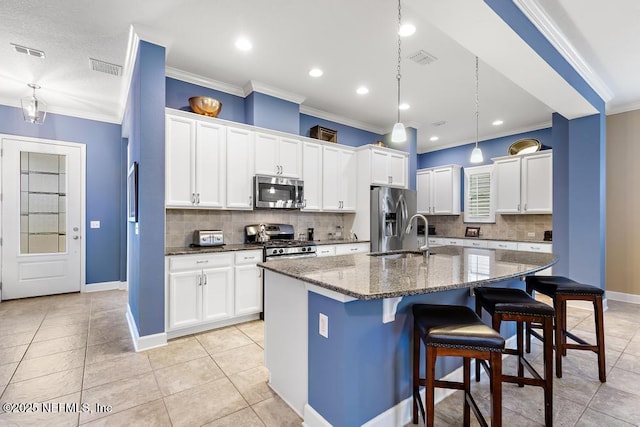 kitchen featuring dark stone countertops, stainless steel appliances, a center island with sink, and white cabinets